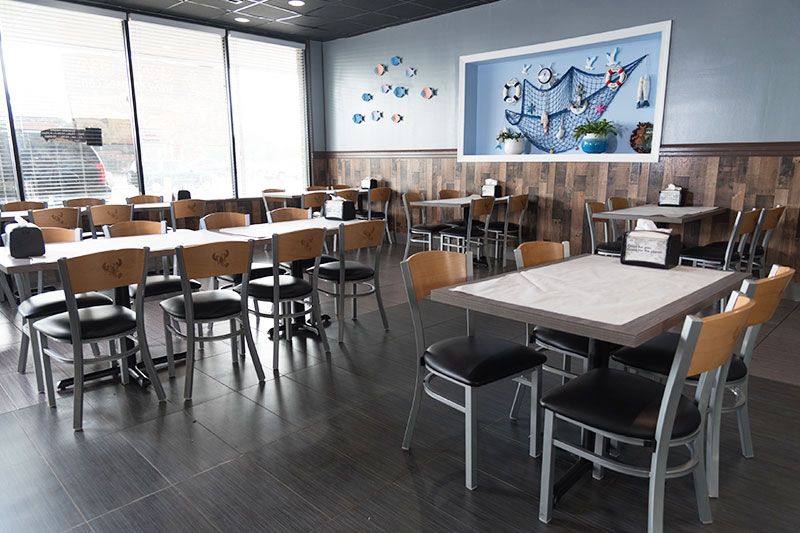 Empty restaurant dining room with tables, chairs, and large windows letting in daylight