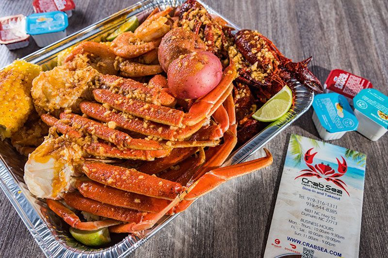 Tray of cooked crab legs and seafood with lemon wedges and sauces on a table