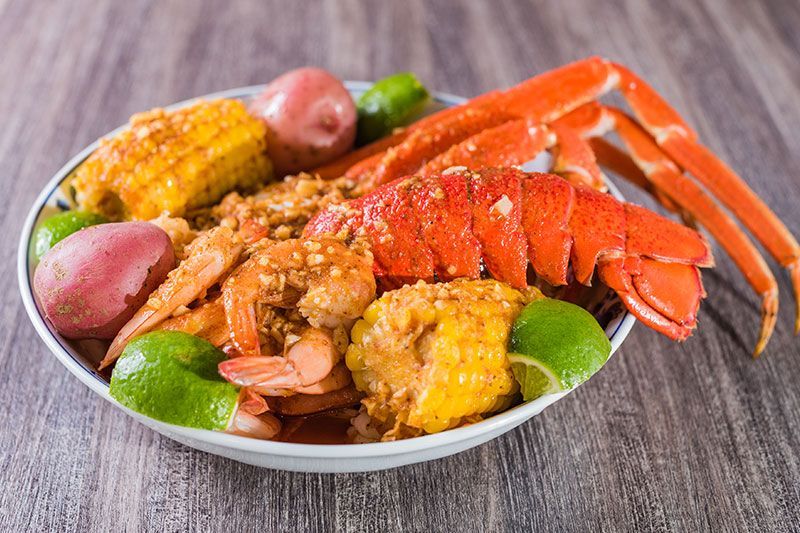 Seafood platter with crab legs, corn, potatoes, lime, and seasoned sauce on a white plate