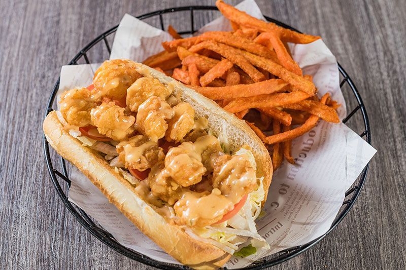 Shrimp po’ boy sandwich with orange fries in a basket lined with parchment paper