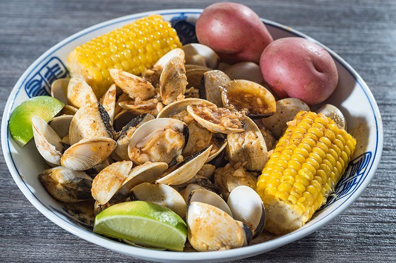 A bowl of clam soup with corn, red potatoes, and lime wedges