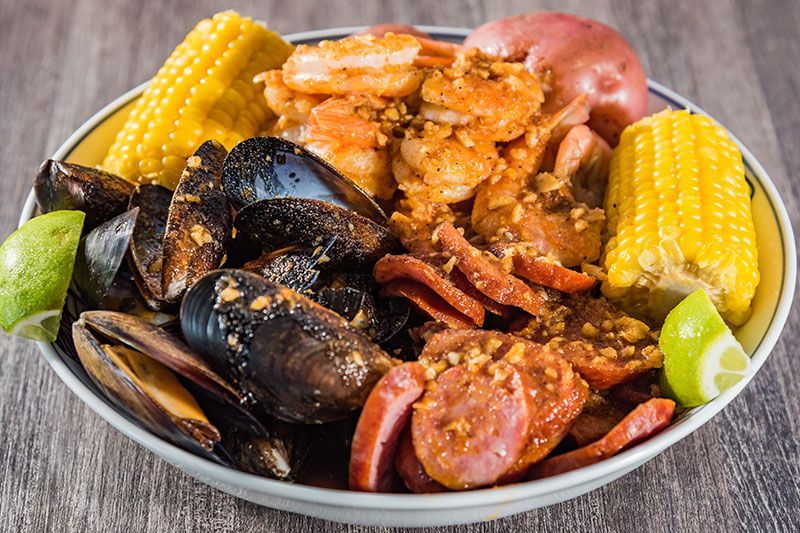 Seafood boil with crab legs, mussels, corn, potatoes, sausage, and lime wedges in a bowl