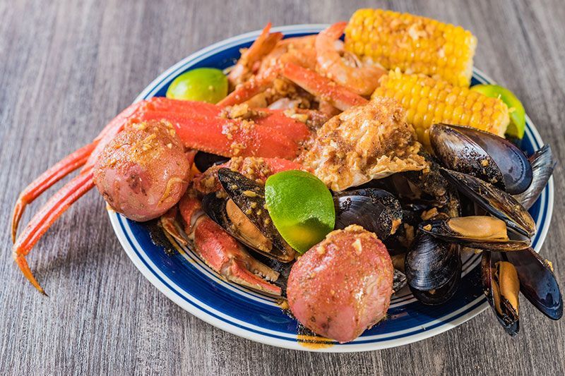 Seafood platter with crab legs, mussels, shrimp, corn, and lime on a blue plate