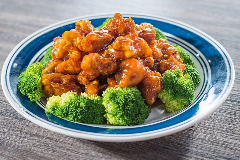 Glazed orange chicken on a blue plate, garnished with broccoli florets