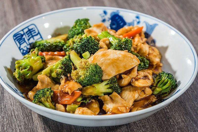 Bowl of stir-fried chicken and broccoli with carrots in a savory sauce on a wooden table