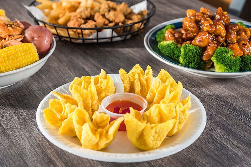 Platter of crab rangoons with dipping sauce, surrounded by corn, fried chicken, and broccoli on a table