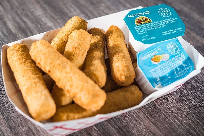 Fried fish sticks in a tray with two blue dipping sauce cups on a wooden table