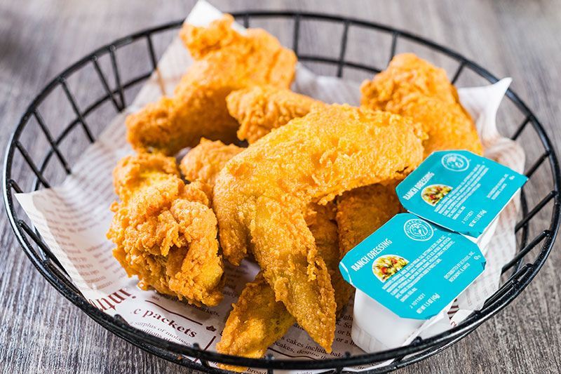 Fried chicken pieces in a black basket with blue dipping sauce packets