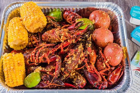 Aluminum tray of spicy crawfish with corn, potatoes, and lime wedges