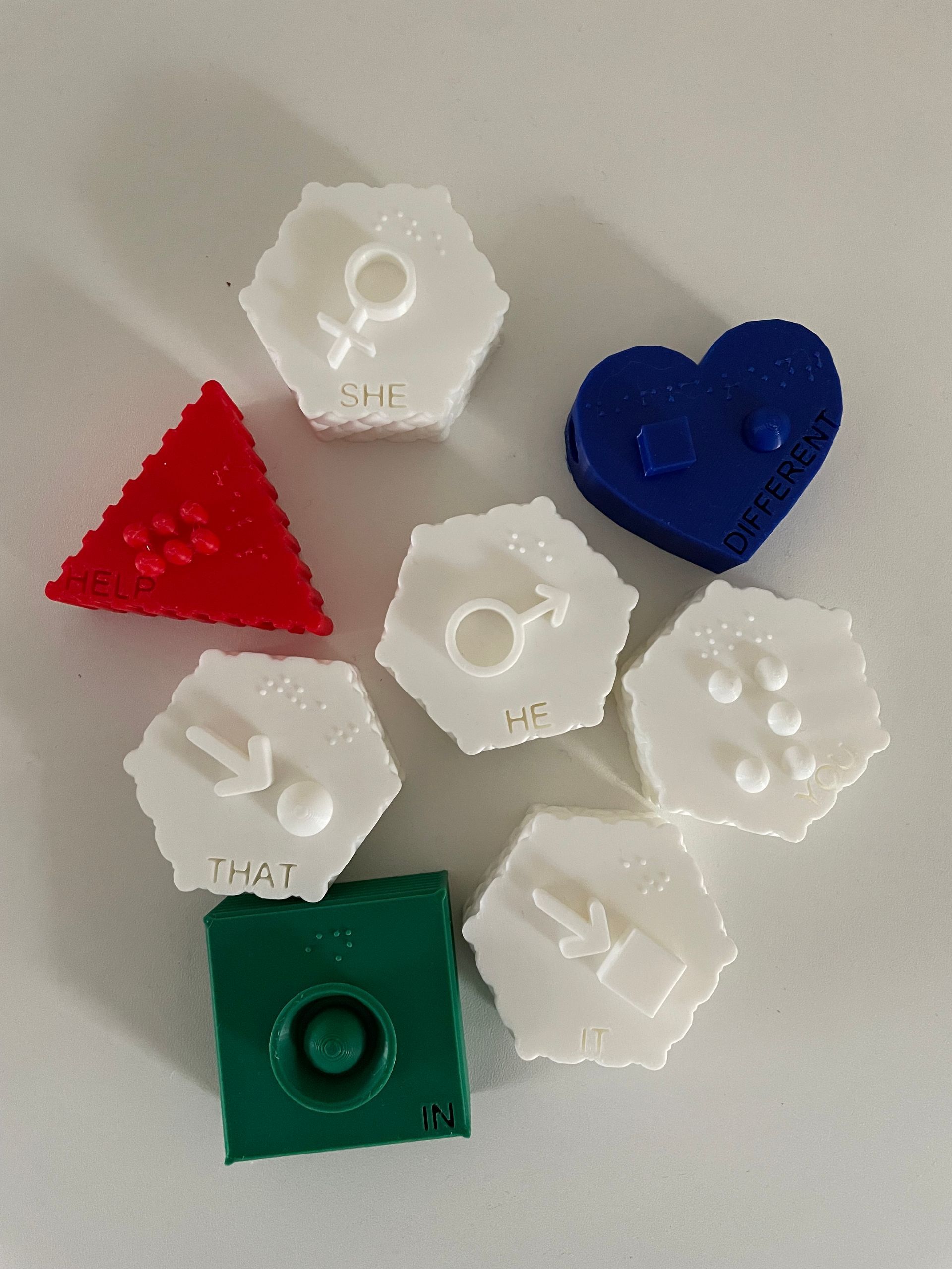 Various colorful 3D-printed shapes: red triangle, blue heart, white hexagons with symbols, and green square.