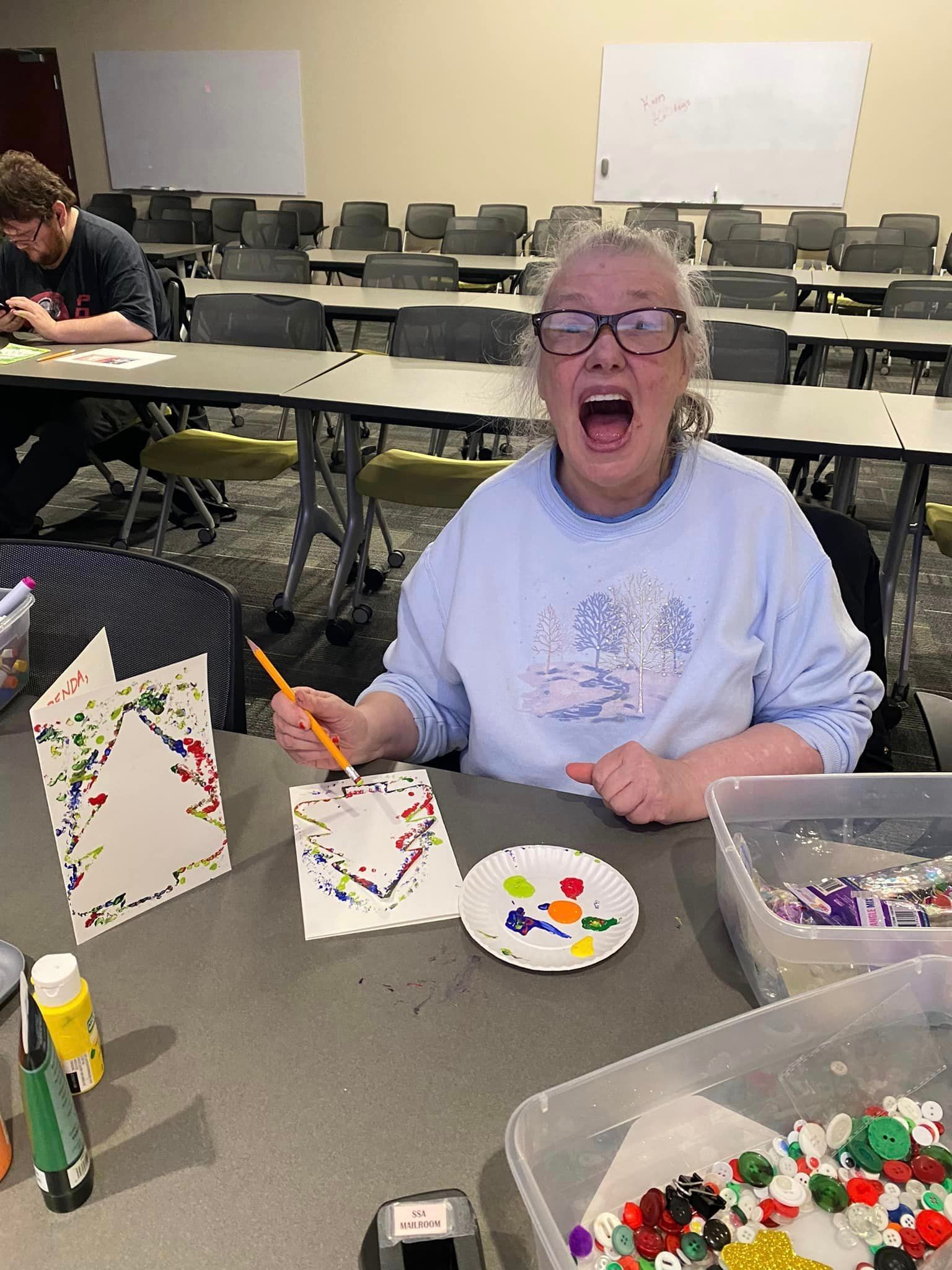 Woman with mouth open, painting a card, art room setting.