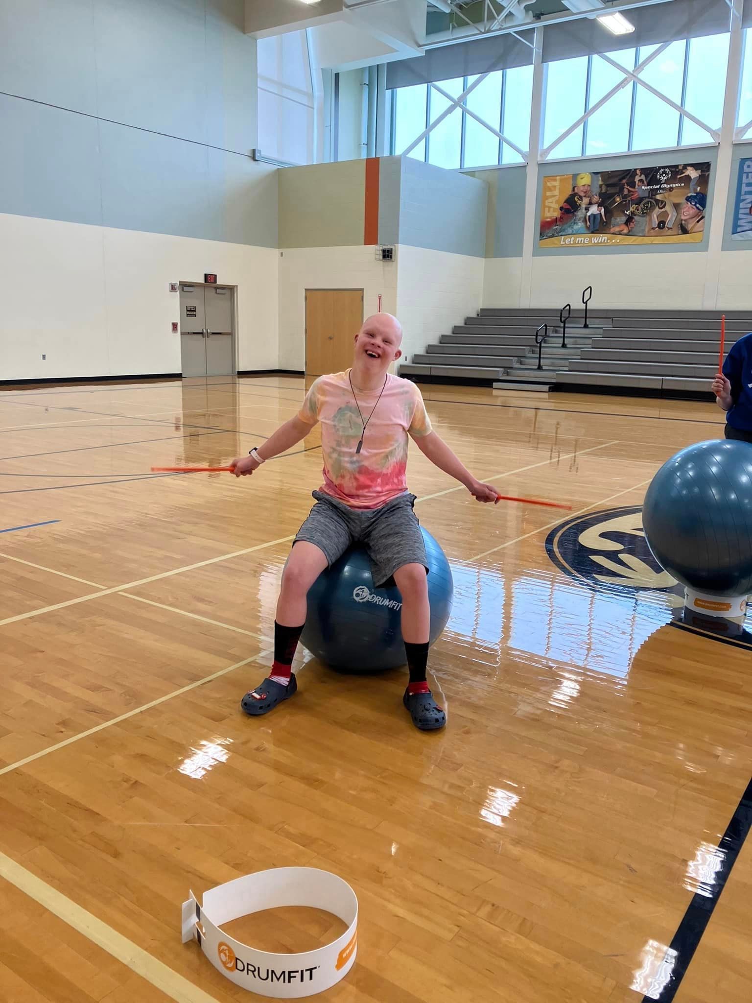 Person on exercise ball in gym, arms outstretched, holding sticks.