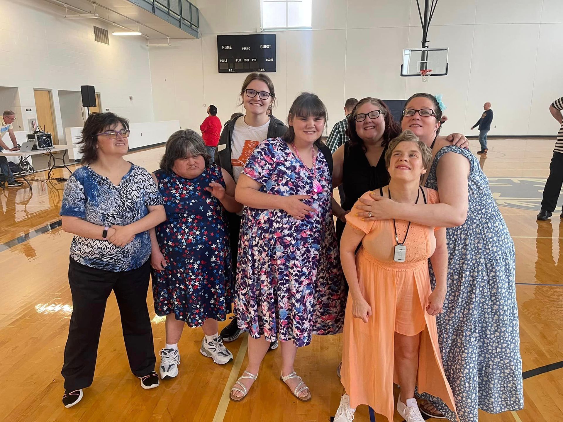 Group of women smiling, posing in a gymnasium. Several are wearing dresses.