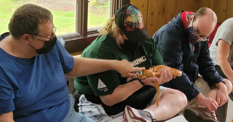 People holding an orange salamander indoors, wearing masks. One person points, others watch.