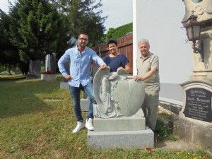 Drei Menschen stehen neben einer Statue auf einem Friedhof.