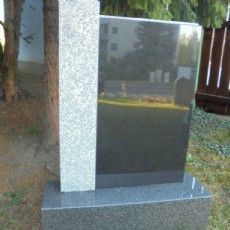 Ein schwarz-weißer Grabstein steht neben einem Baum auf einem Friedhof.