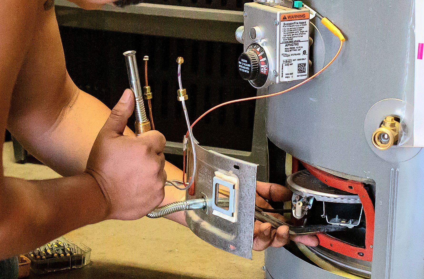 Person repairing a water heater, holding parts and tools near the unit's access panel.