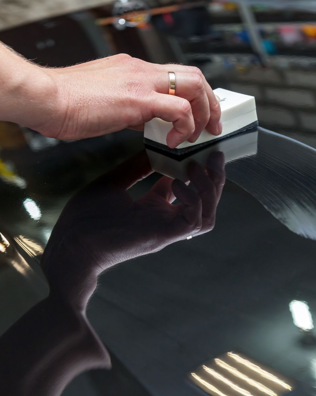 A person is using a blue squeegee to remove plastic from the hood of a car