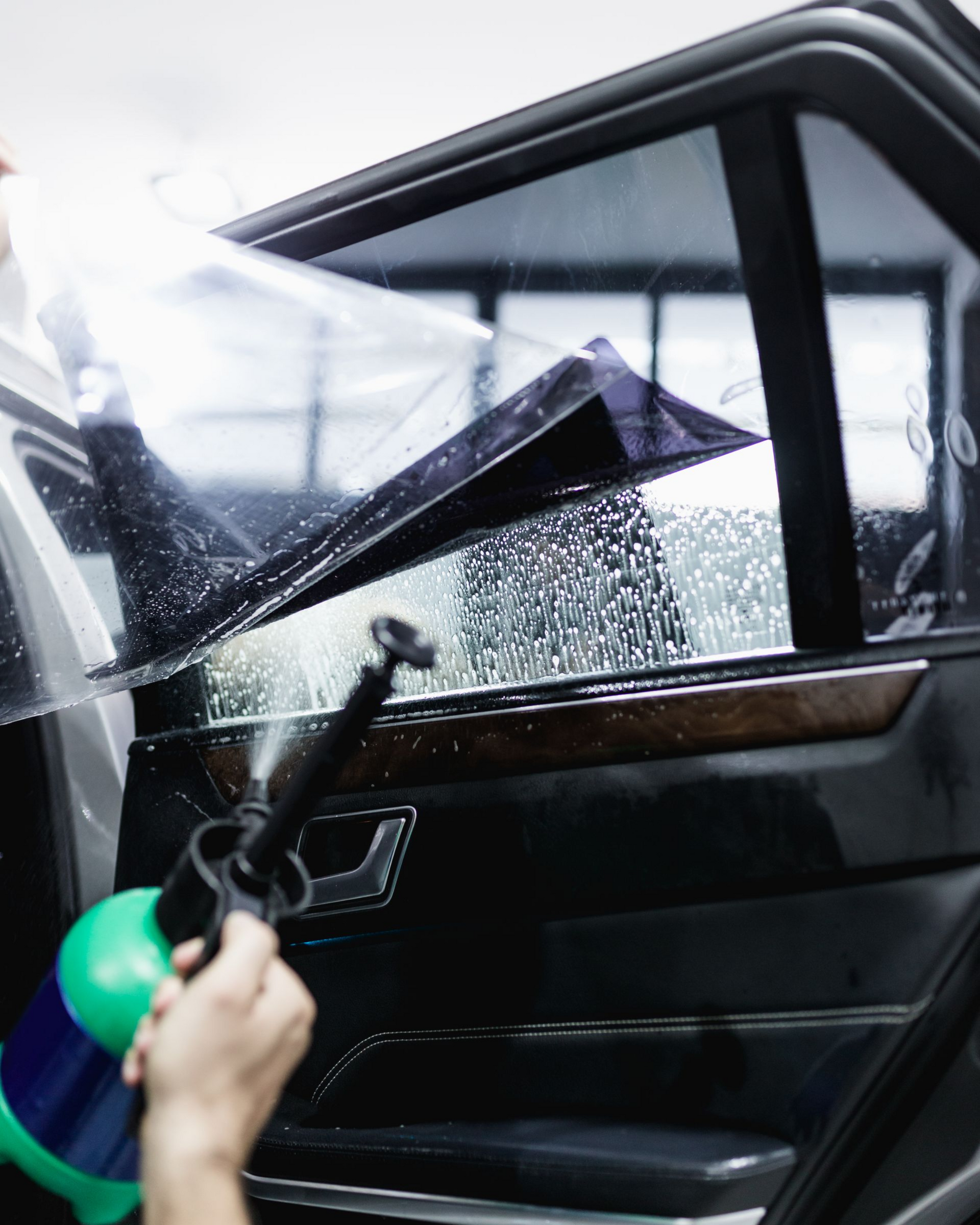 Person applying tint film to a car window with a spray bottle.