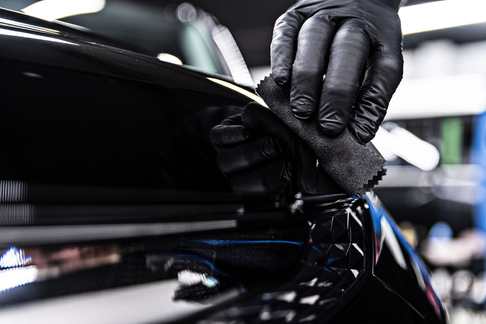 Gloved hand applying a detailing product to a shiny black car with a black applicator.