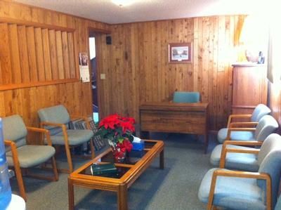 Small waiting room with wood-paneled walls, blue chairs, wooden table, and red poinsettia centerpiece.