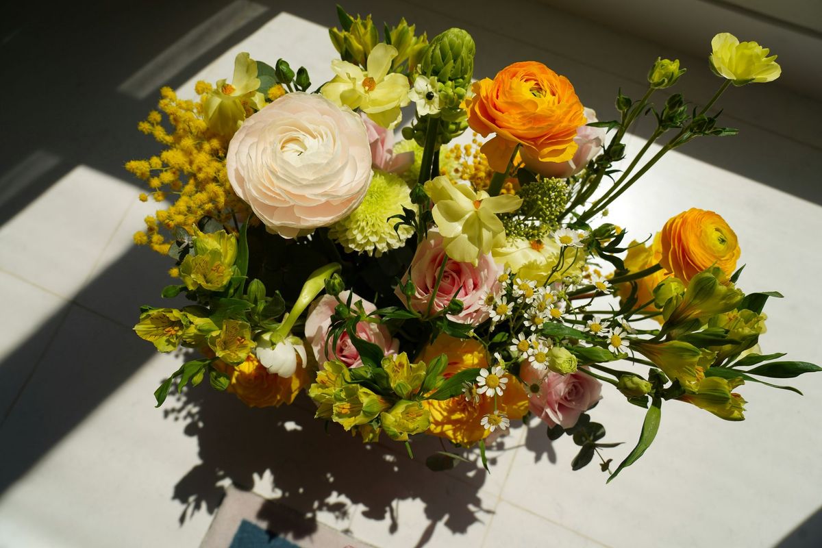 Mixed bouquet of white, yellow, and orange flowers on a sunlit table