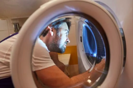 Un hombre está mirando la puerta de una lavadora.