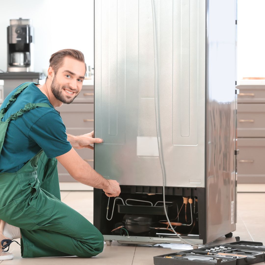 Un hombre está arrodillado frente a un refrigerador en una cocina.