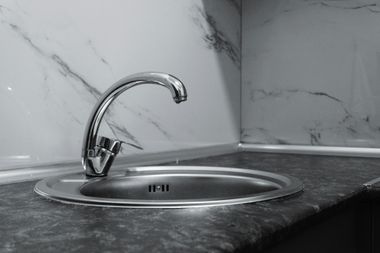 A chrome kitchen faucet installed over a circular stainless steel sink set into a dark gray marble-patterned countertop.