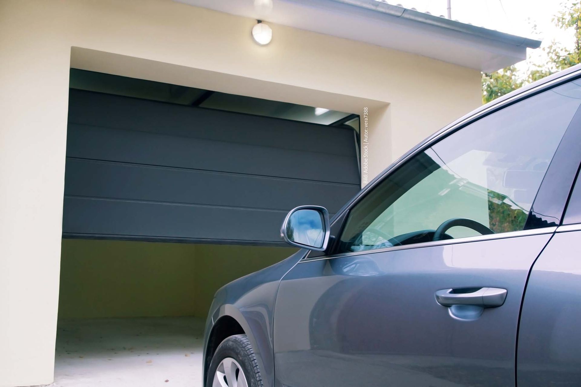 Ein Auto steht mit geöffneter Tür in einer Garage. Garagentor von Terrassenwelten Frank Merz