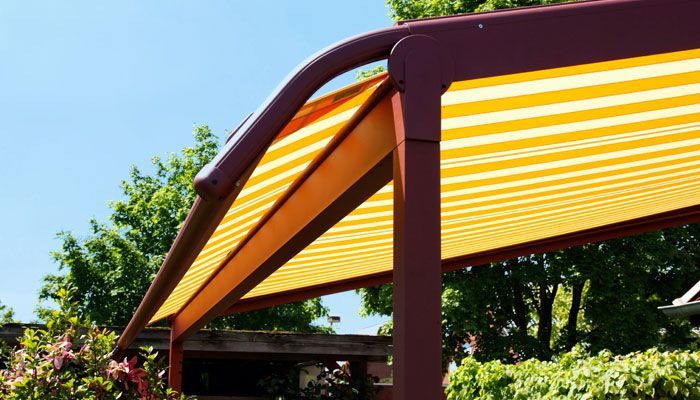 Eine gelb und orange gestreifte Markise auf einer Terrasse mit Bäumen im Hintergrund