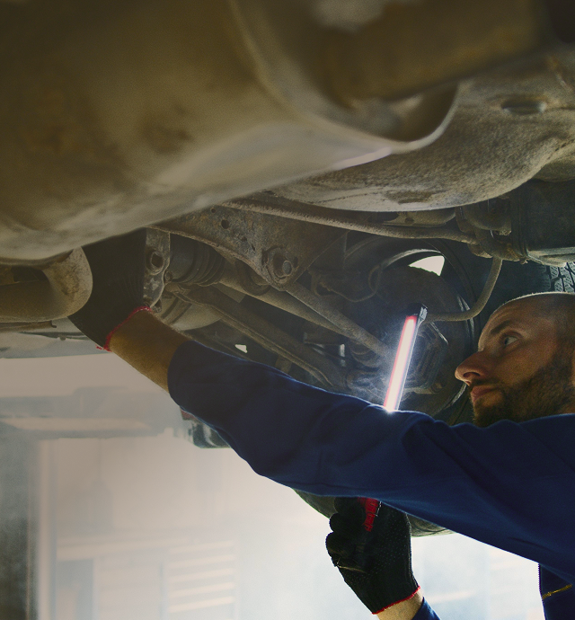 Mechanic inspecting a car’s underside with a flashlight in a garage | Len's Automotive
