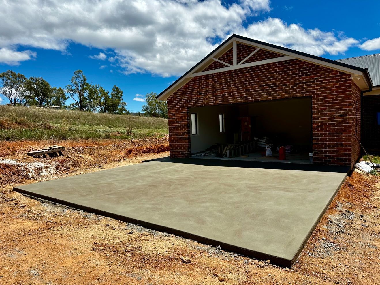 A Trowel Is Sitting On A Concrete Surface Next To A Wheelbarrow — Regional Concreting Solutions In Blayney, NSW