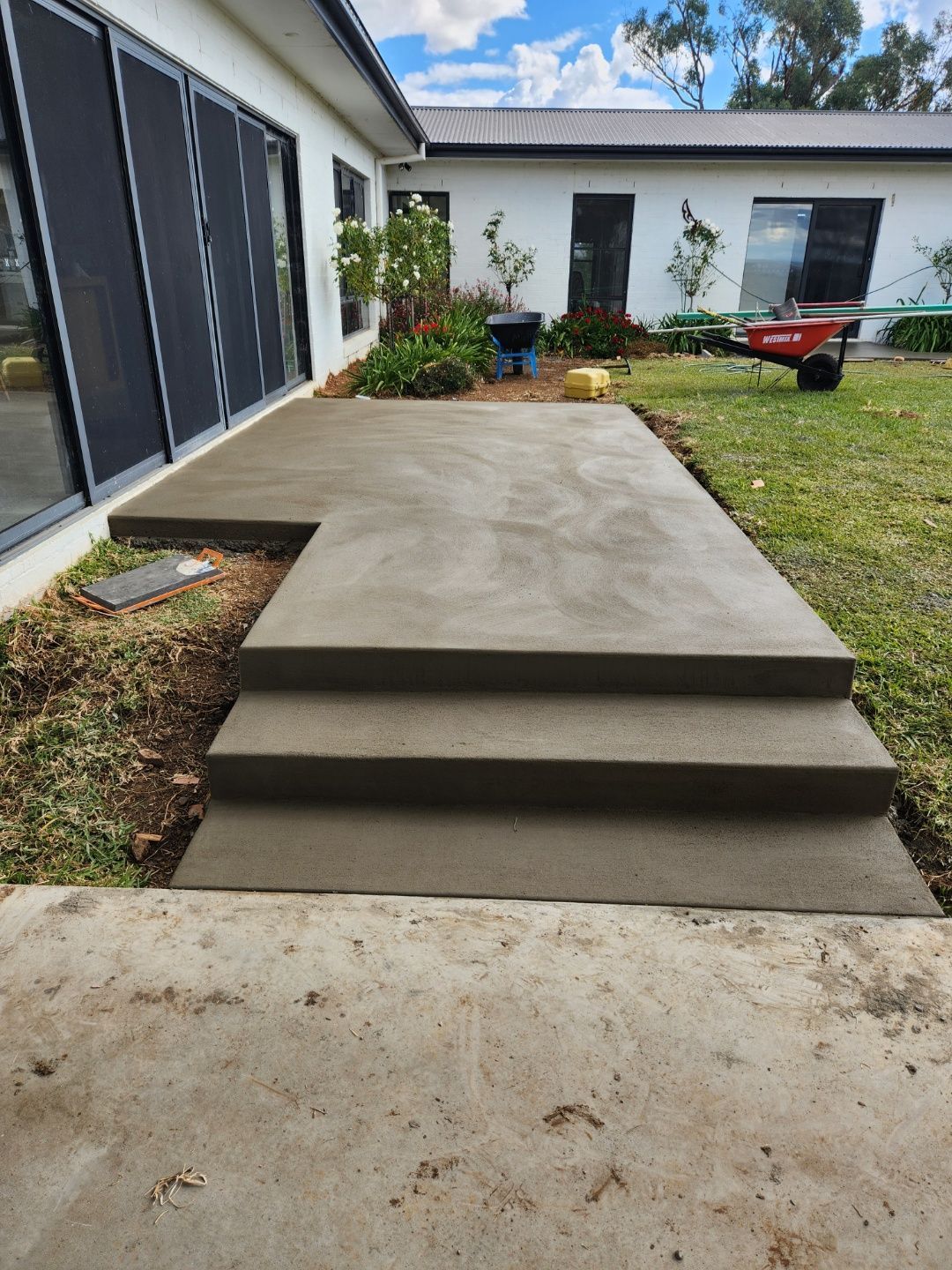 A Man Is Using A Trowel To Spread Concrete On A Sidewalk — Regional Concreting Solutions In Molong, NSW