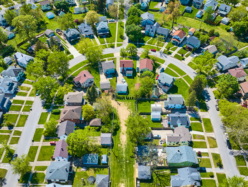 Aerial view of a residential neighborhood with houses, lawns, and tree-lined streets beside a company logo. Aerial view of a residential neighborhood with houses, lawns, and tree-lined streets beside a company logo.
