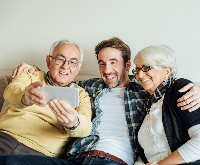 Three smiling people on a couch taking a selfie, with one holding a tablet.