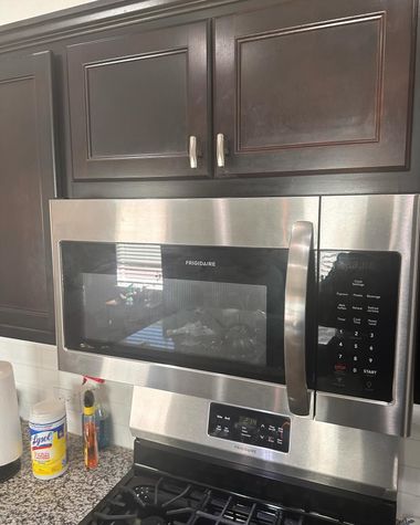 A stainless steel over-the-range microwave mounted beneath dark wood cabinets above a gas stovetop in a kitchen.