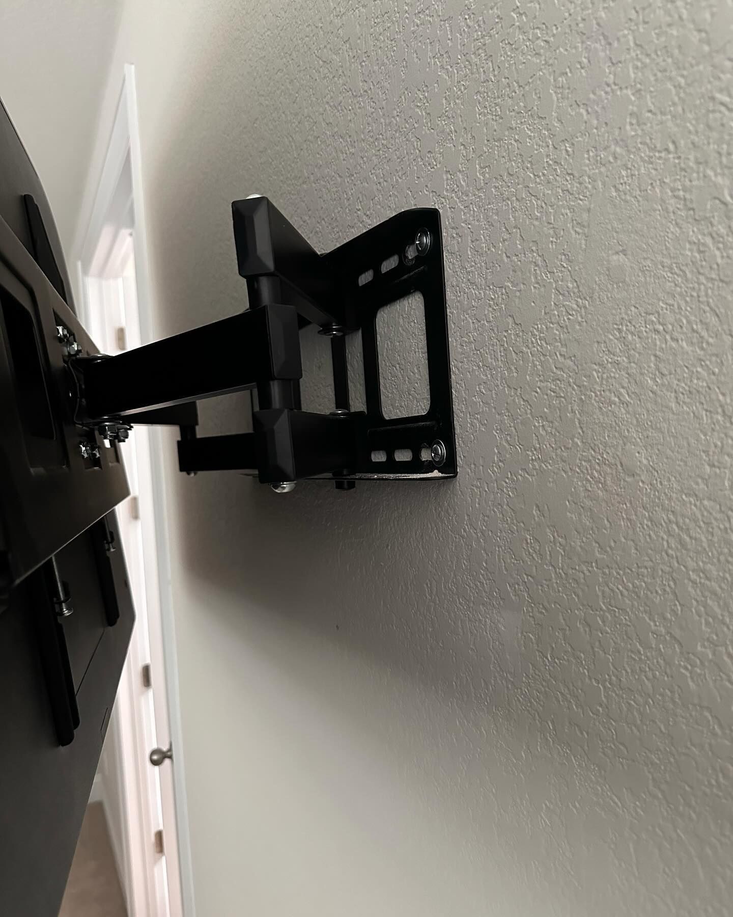 A black, articulated full-motion TV wall mount installed on a textured, light gray wall.