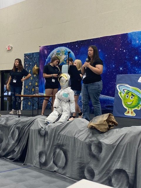 A group of people standing in front of a stage with a green alien on it