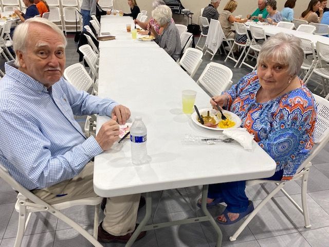 A man and a woman are sitting at a long table eating food