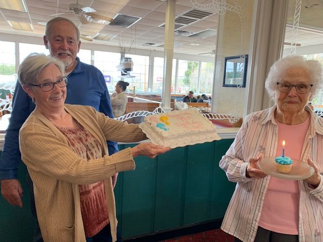 Two elderly women are holding a cake and a cupcake with a lit candle.