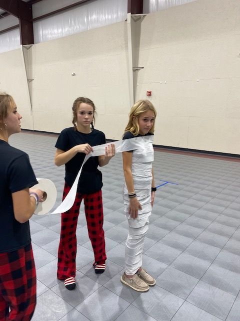 A girl wrapped in toilet paper is standing next to two other girls