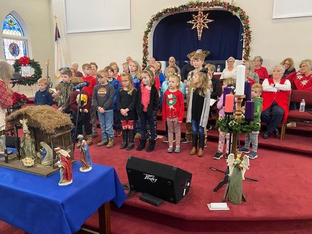 A group of children are singing in front of a nativity scene in a church.