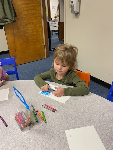 A little girl sits at a table with a bag of crayons