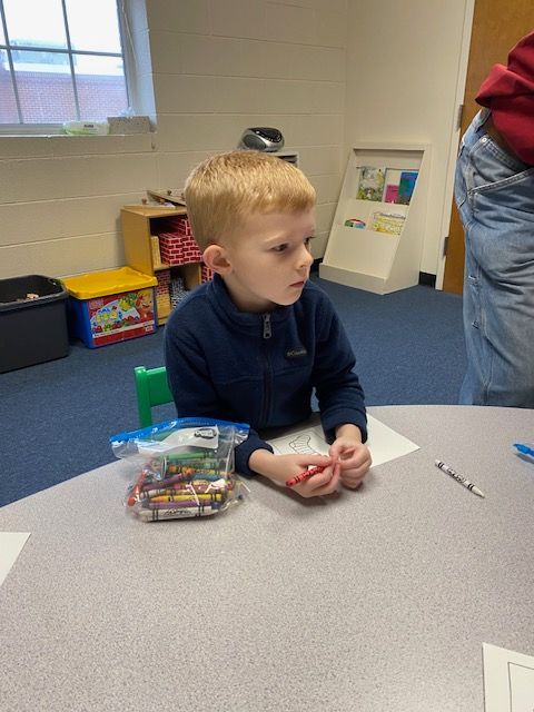 A young boy sits at a table with a bag of crayons
