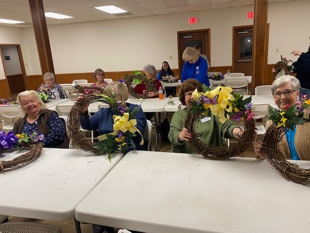 A group of women are sitting at tables making wreaths.
