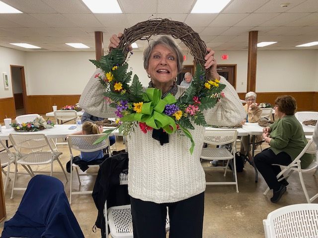 A woman in a white sweater is holding a wreath over her head.