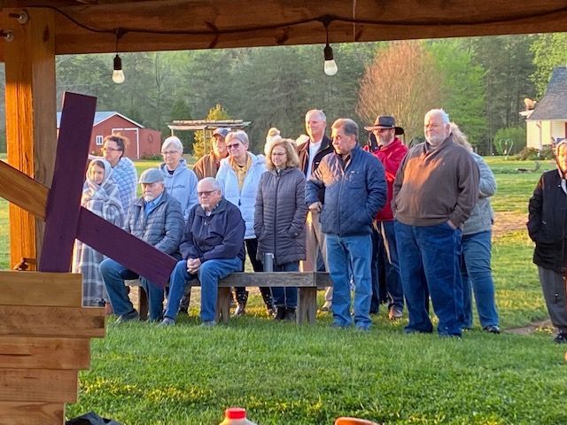 A group of people are standing around a wooden cross in a field.