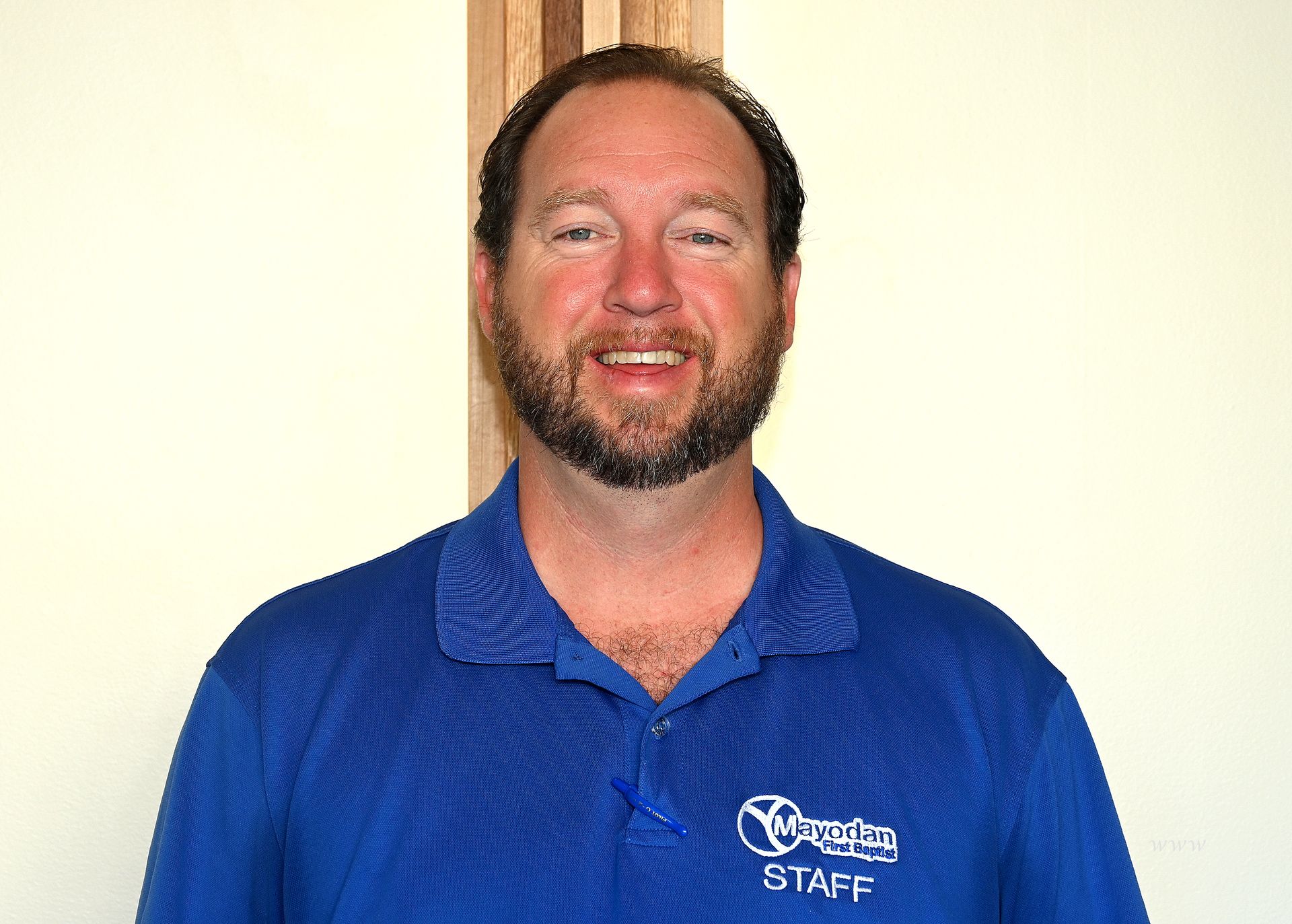 A man with a beard wearing a blue staff shirt