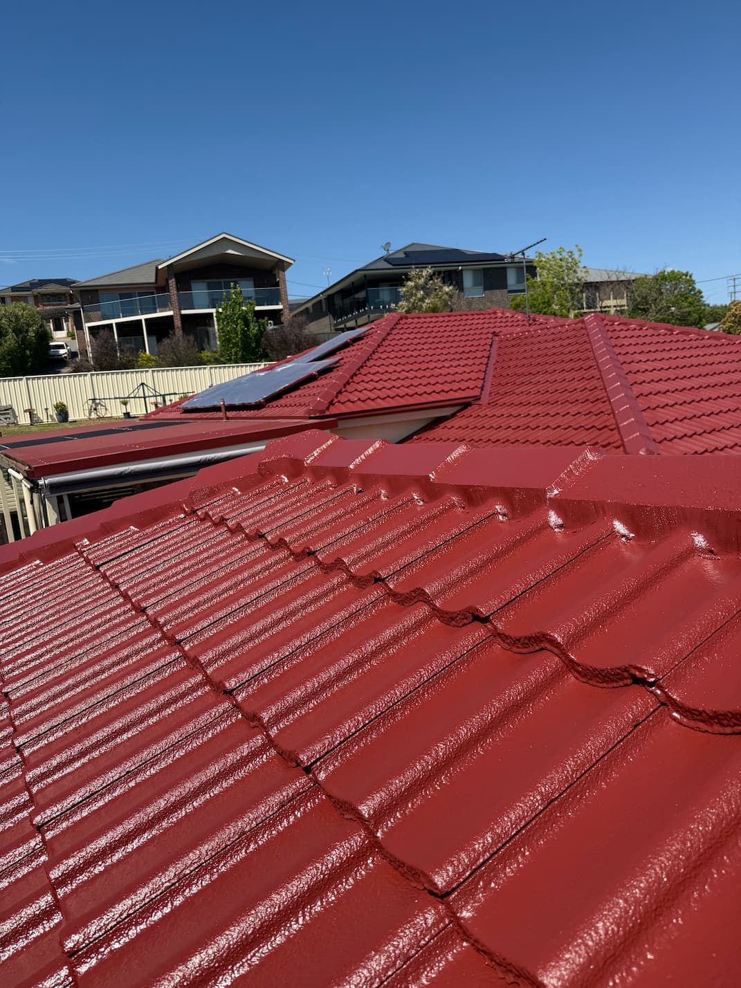 Red tiled roof under a clear blue sky, with neighboring houses in the background
